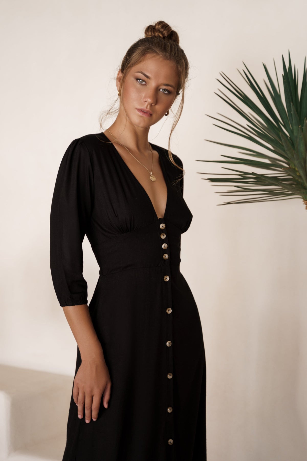 Woman wearing a black dress with buttons against a neutral background