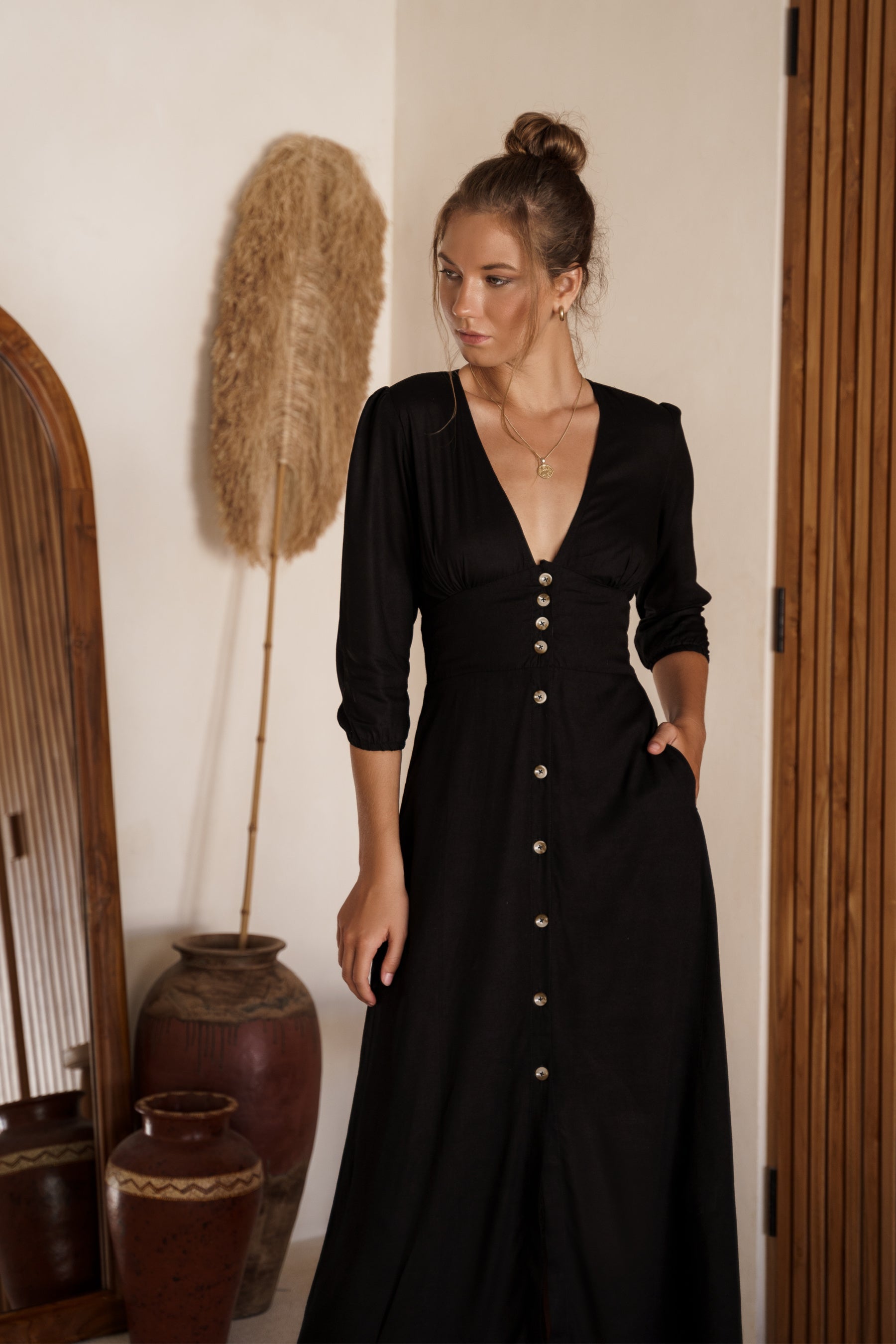 Woman wearing a black dress with buttons in a room with decorative elements.