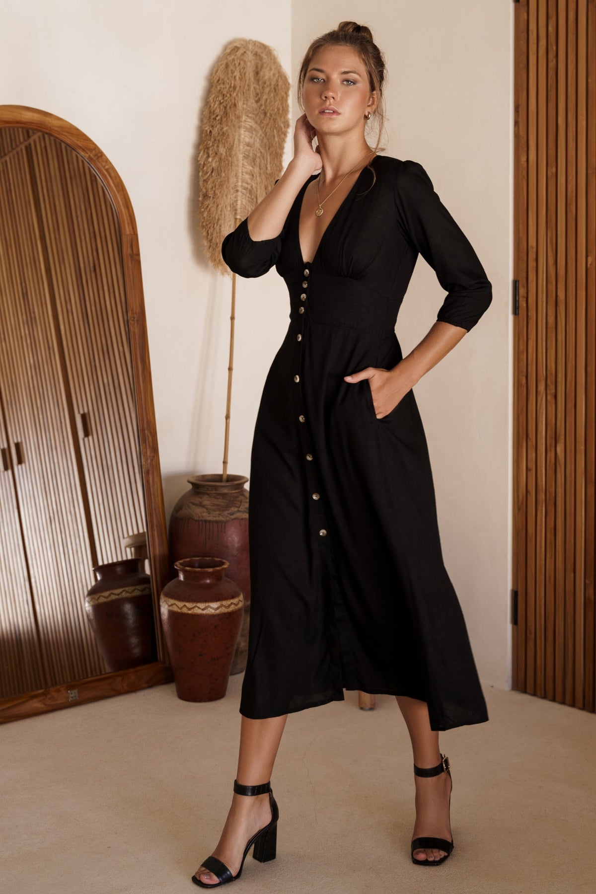 Woman wearing a black dress in an indoor setting with wooden furniture and decor.