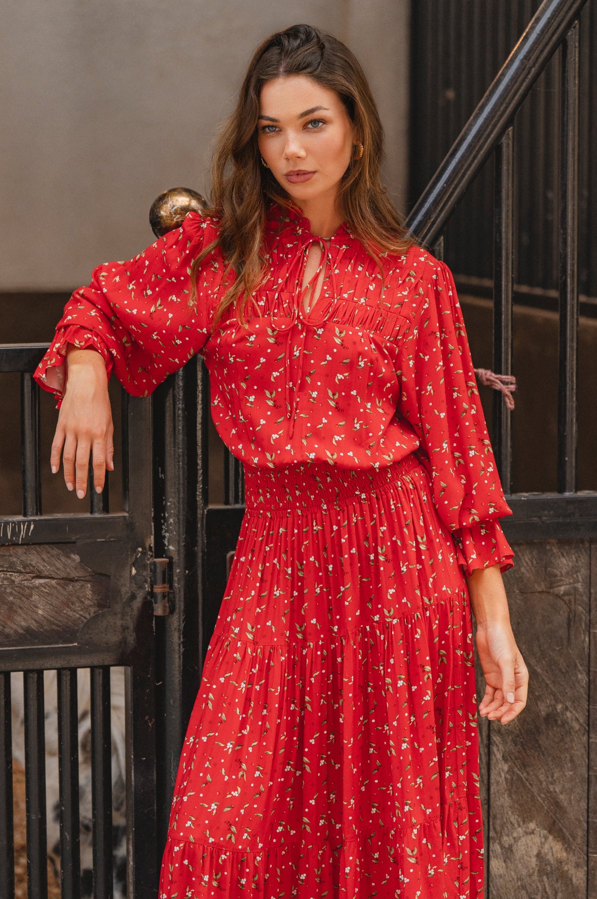 Woman wearing a red dress with a floral pattern standing against a dark metal gate.