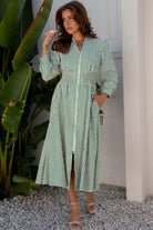 Close-up front view of model wearing green and white striped dress with V-neckline and cuffed sleeves.
