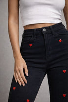 Black jeans with red heart patterns worn by model on a gray background