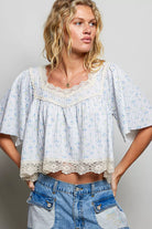 Model wearing the Bluebell Lace Flutter Top featuring textured fabric, delicate blue floral print, scalloped lace neckline, flutter sleeves, and lace hem, AVAH
