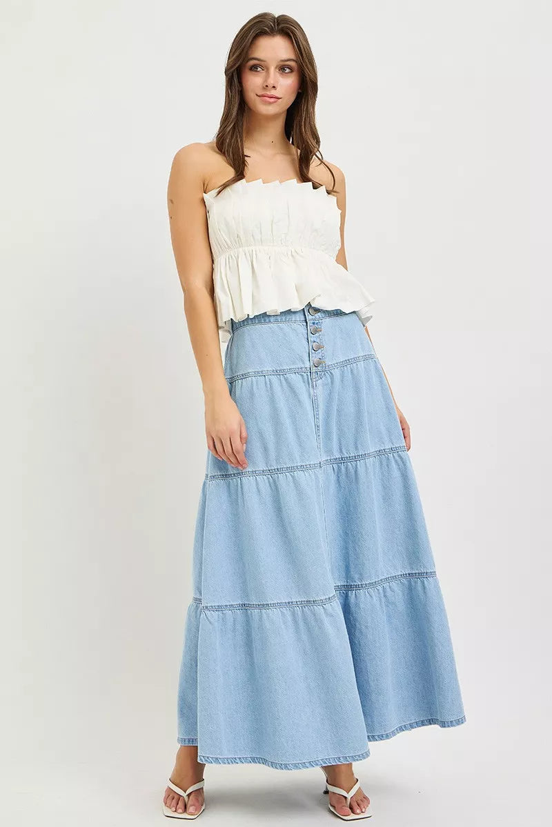 Woman wearing light wash tiered denim maxi skirt with white strapless top front view
