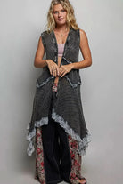 Woman wearing a vintage washed black sleeveless open crochet vest with mixed knit textures, lace ruffle trim, and an asymmetrical handkerchief hem layered over a neutral bralette and dark denim.