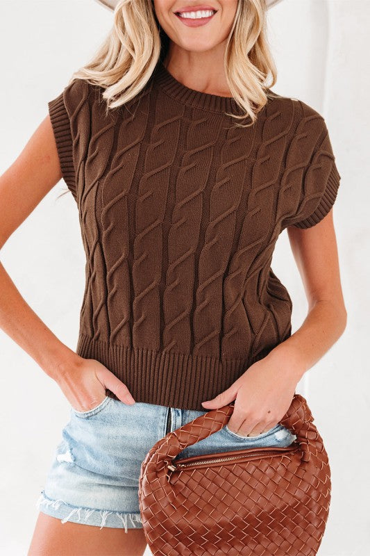 Front view of brown cable knit sleeveless top styled with light denim shorts and woven bag.
