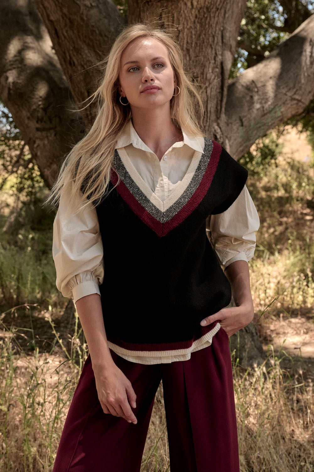Woman wearing a black sweater vest over a cream blouse with burgundy pants