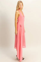 Side view of pink chiffon halter midi dress with rosette hip detail and asymmetrical draped hem

