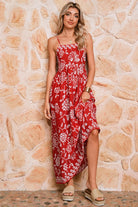 Woman wearing a red floral dress standing against a stone wall.