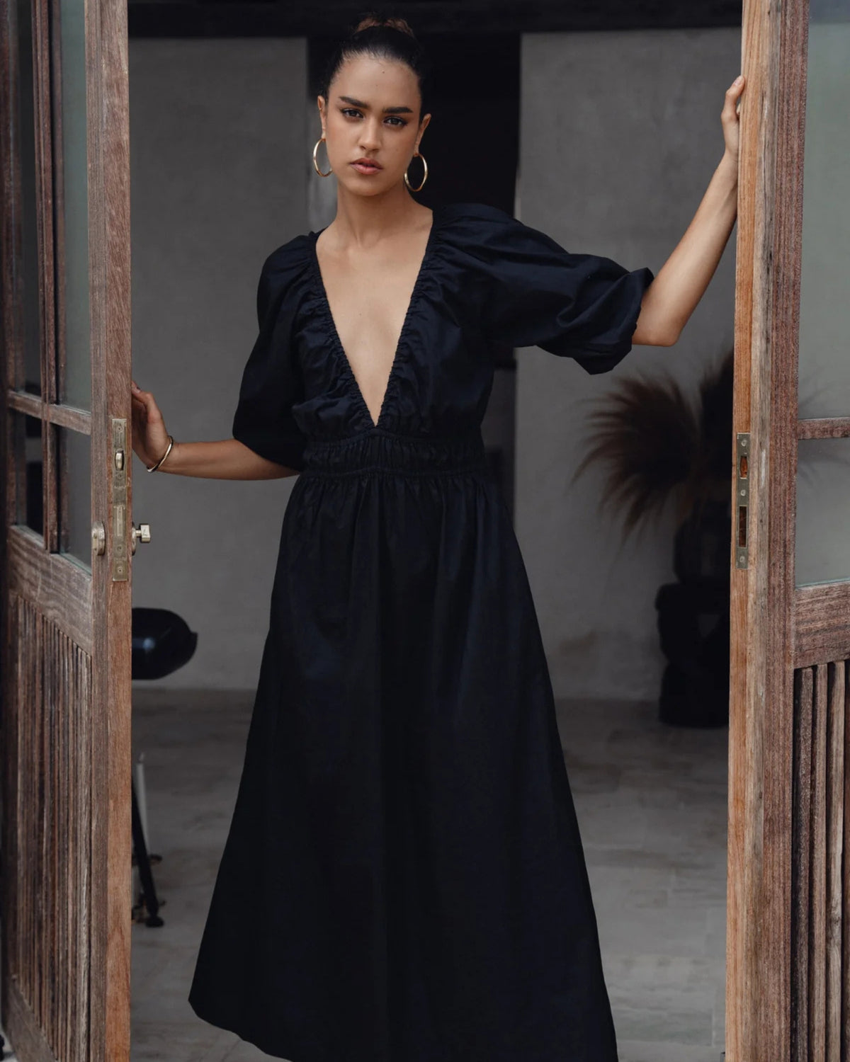 Model wearing a black Bali ELF maxi dress in a wooden doorway