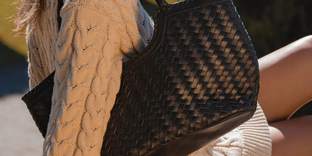 Close up of a dark woven Bali ELF leather bag with a cream cable knit sweater