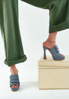 Blue denim high-heeled shoes worn with green pants on a white background 