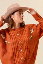 Close up of Copper Meadow Floral Knit Sweater showing cream and orange embroidered flowers and textured cable knit detailing.