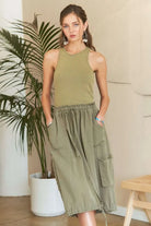 Model wearing an olive green mixed media cargo midi dress with a ribbed tank bodice, cargo pockets, drawstring waist, and adjustable drawstring hem.