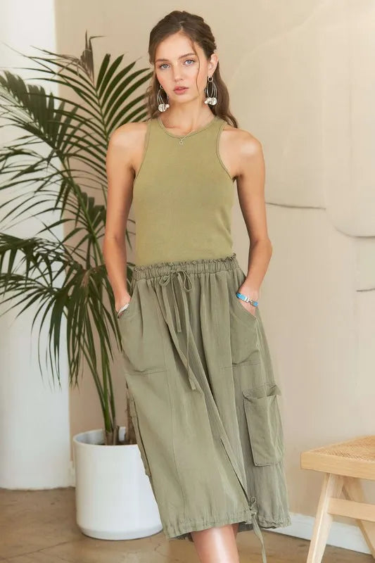 Model wearing an olive green mixed media cargo midi dress with a ribbed tank bodice, cargo pockets, drawstring waist, and adjustable drawstring hem.