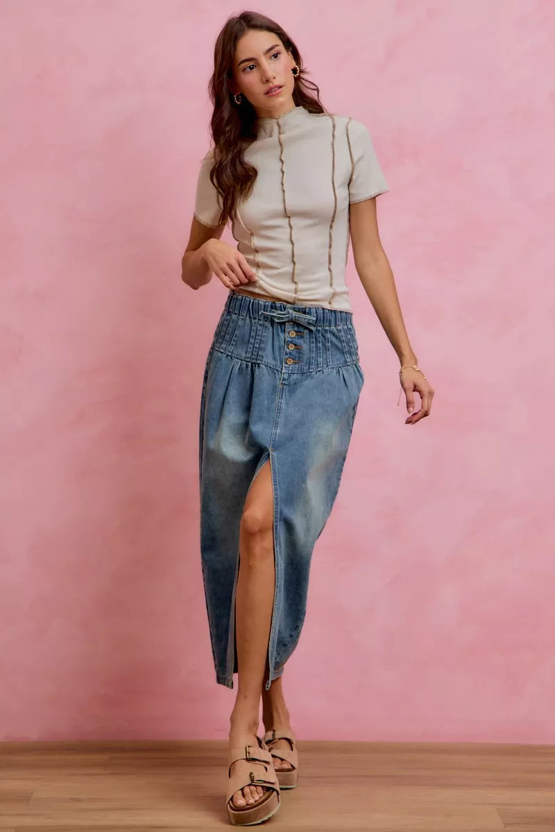 Model wearing the AVAH Marlowe Button Front Denim Midi Skirt in a soft washed denim with a paperbag waistband, button front detail, self tie waist, and front slit, styled with a fitted short sleeve top and platform sandals.