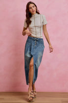 Model wearing the AVAH Marlowe Button Front Denim Midi Skirt in a soft washed denim with a paperbag waistband, button front detail, self tie waist, and front slit, styled with a fitted short sleeve top and platform sandals.