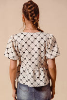 Back view of cream textured peplum blouse with puff sleeves and black bow detail accents | AVAH Collections