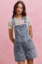AVAH-Model wearing washed light denim button front denim shortalls layered over a cream lace short sleeve top 