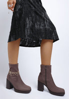 Taupe ankle boots worn with a black crushed velvet dress on a white background