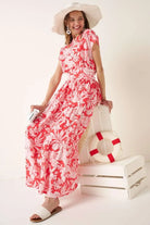 Coral floral two piece maxi skirt set featuring a short sleeve top with waist tie detail and tiered maxi skirt styled with a wide brim hat.