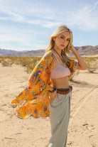 Mustard tropical print kimono flowing in the wind, styled with a bralette and sage green pants