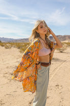 AVAH-Model wearing mustard yellow tropical print kimono with flowing sleeves in a desert landscape.