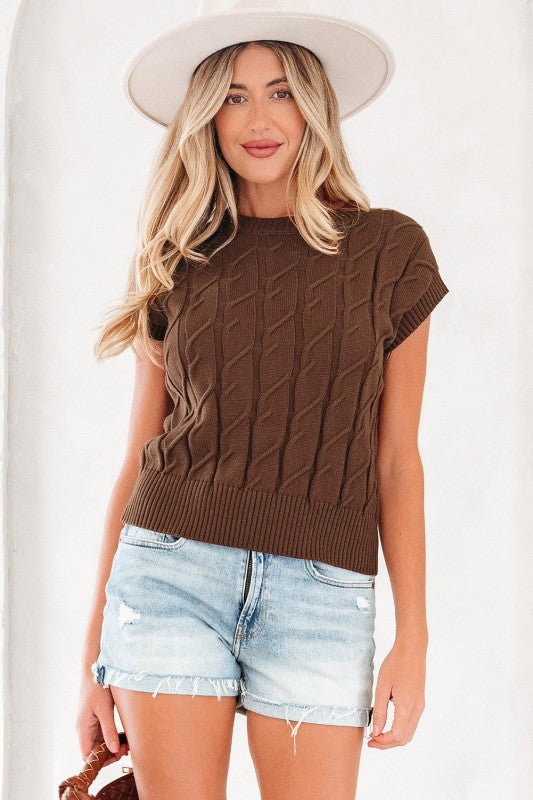 Full front view of brown sleeveless knit top on model wearing white hat and denim shorts.