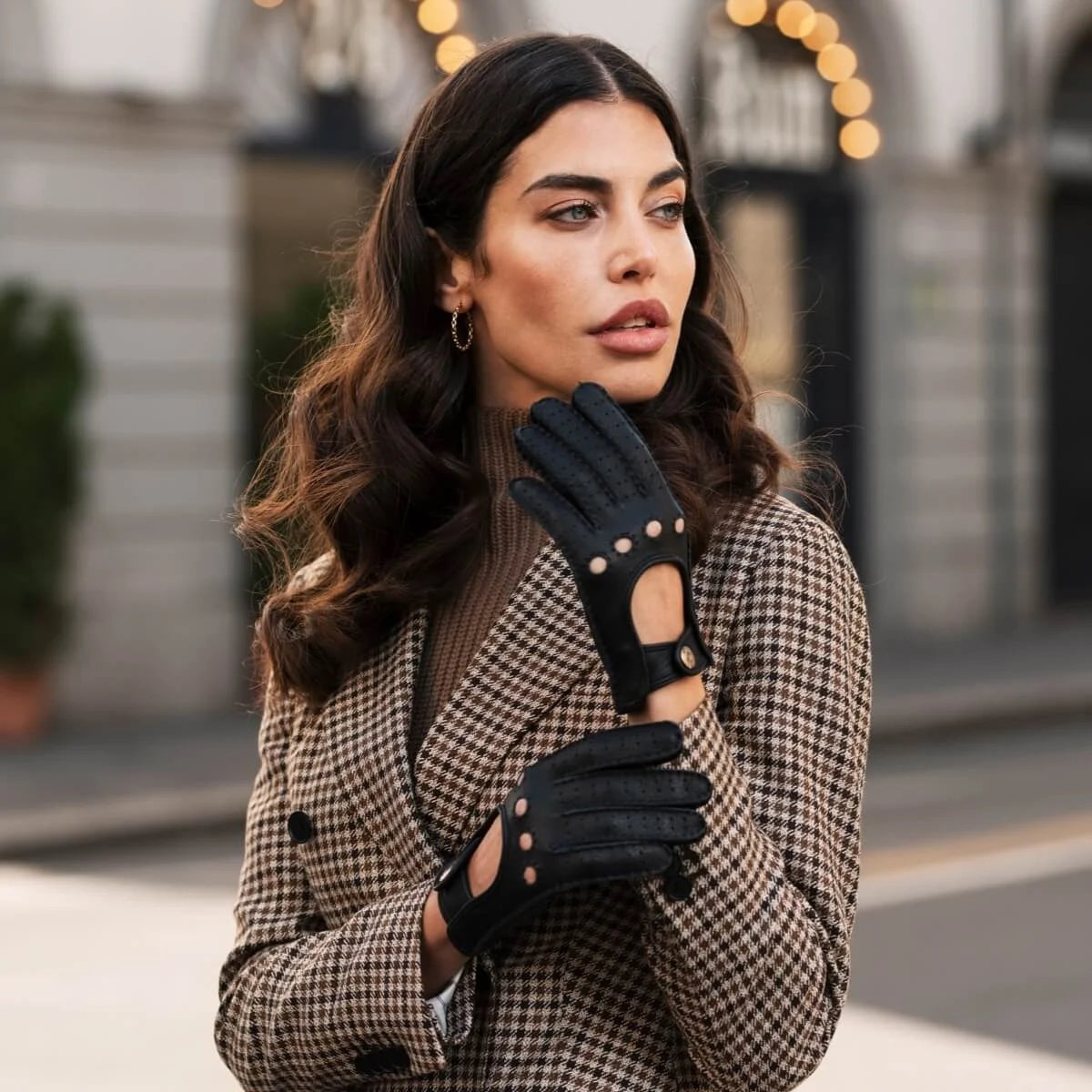 Model wearing black leather driving gloves with cutout details and a checked blazer