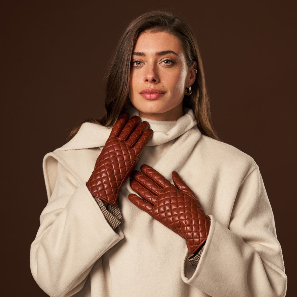 Model wearing quilted cognac leather winter gloves with a cream coat