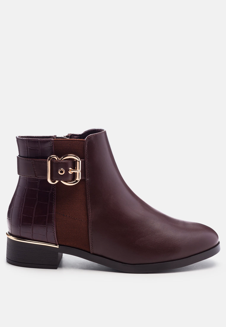 A dark brown leather ankle boot with a side buckle strap, a crocodile-embossed side panel, and a low block heel, shown from a side profile on a light gray background.