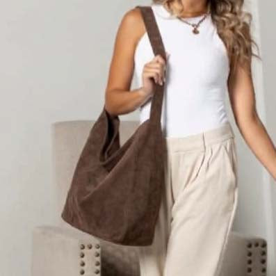 A woman wearing a white sleeveless top and beige pants carries a large brown suede hobo shoulder bag.