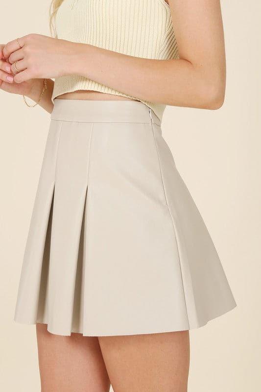 Alexis Pleated Vegan Leather Mini Skirt - Ivory. This vegan leather pleated mini skirt is made of high quality faux leather. The skirt has four pin tucks for each front and back and a side zipper closure. The Alexis Pleated Vegan Mini Skirt will make your legs look longer and slimmer and pairs perfectly with a blouse for work or play! 