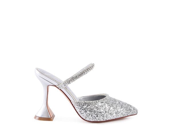 The perfect pair of silver glitter mules with rhinestone embellishment, designed to make you shine. Featuring a sculpted heel, pointed toe and crystal decorated elastic strap. Avah Couture