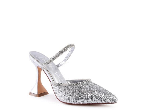 The perfect pair of silver glitter mules with rhinestone embellishment, designed to make you shine. Featuring a sculpted heel, pointed toe and crystal decorated elastic strap. Avah Couture