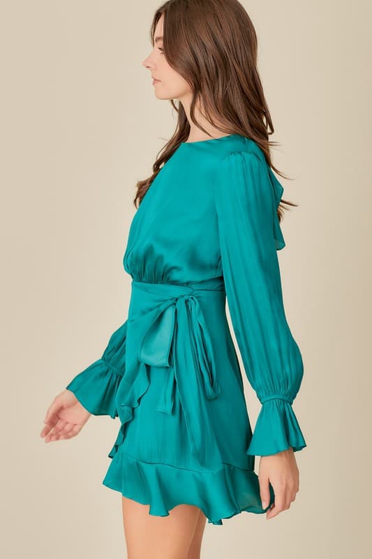 This woven dress is a must have for any woman who loves to look stylish. It features a long sleeve, a belled cuff, back zipper closure, an open back with tie detail, ruffle detail and tie waist styling. Dress it up with strappy heels and jewelry or wear it casually with flats. Avah Couture