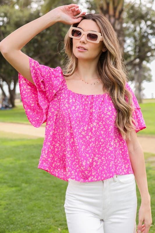 Avah Couture- Make a sweet impression in this smocked square neck blouse covered in delightful blooms. This fuchsia floral top has a self-tie open back and short sleeves accented with ruffles. Embrace the phenomenal florals of spring.  Floral print Smocked square neck Ruffle short sleeves Open back with self-tie Short length- Fuchsia Pink 