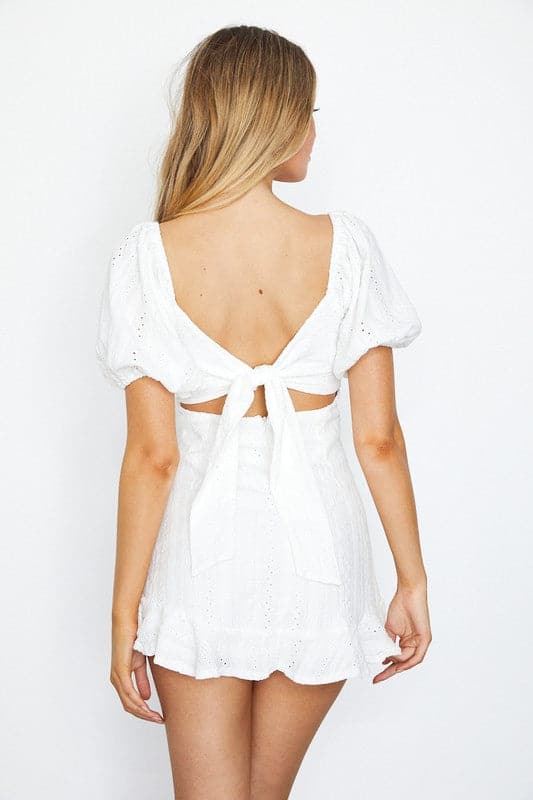 This cute dress is perfect for any spring or summer day. The white mini dress features a textured eyelet design and puff-sleeves for a playful look. The empire waist, tied front and tied open back detailing gives it a feminine silhouette that is sure to look great on any body type - Avah Couture