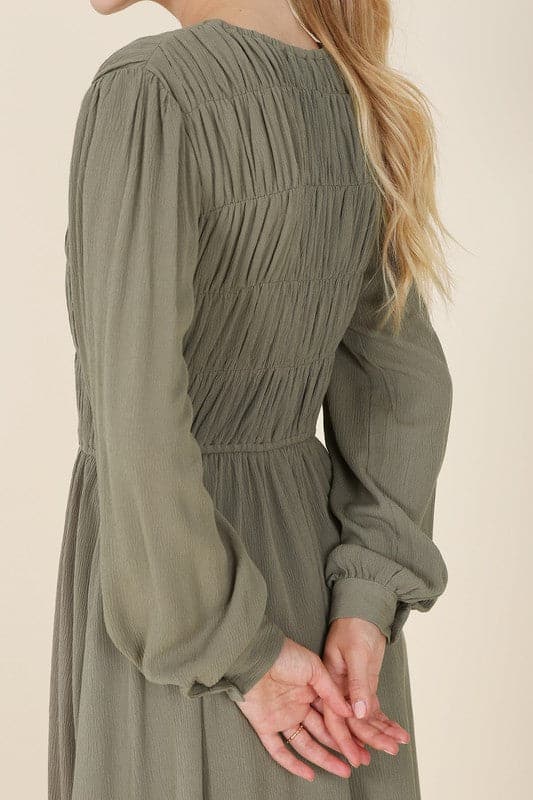This beautiful midi dresses has four tiers of elastic bands at the bodice which creates a lovely ruched effect. This design gives it an elegant and feminine appearance. The All Dressed Up Ruched Midi Dress has a boat neckline, long sleeves with button at each cuff and below the knee length for easy transition into fall. Wear it with heels and a clutch bag for a chic look. This dress is lined.  