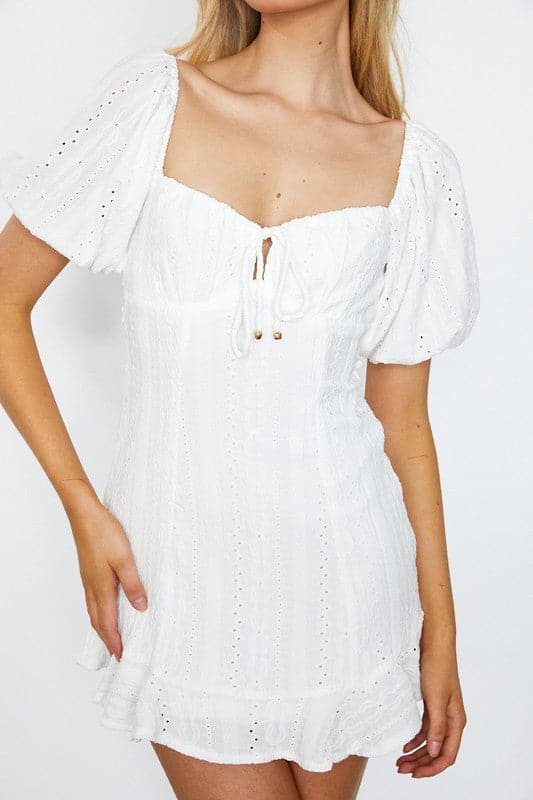 This cute dress is perfect for any spring or summer day. The white mini dress features a textured eyelet design and puff-sleeves for a playful look. The empire waist, tied front and tied open back detailing gives it a feminine silhouette that is sure to look great on any body type - Avah Couture