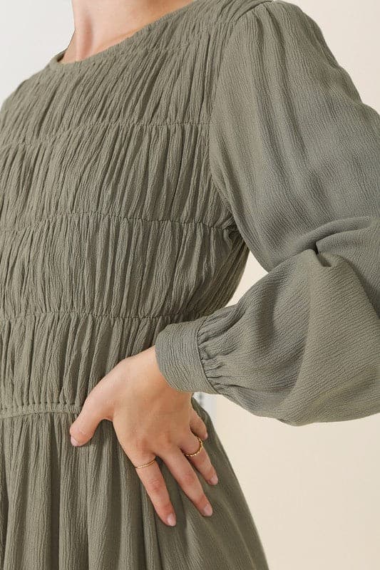 This beautiful midi dresses has four tiers of elastic bands at the bodice which creates a lovely ruched effect. This design gives it an elegant and feminine appearance. The All Dressed Up Ruched Midi Dress has a boat neckline, long sleeves with button at each cuff and below the knee length for easy transition into fall. Wear it with heels and a clutch bag for a chic look. This dress is lined.  
