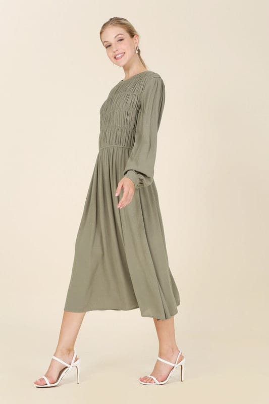 This beautiful midi dresses has four tiers of elastic bands at the bodice which creates a lovely ruched effect. This design gives it an elegant and feminine appearance. The All Dressed Up Ruched Midi Dress has a boat neckline, long sleeves with button at each cuff and below the knee length for easy transition into fall. Wear it with heels and a clutch bag for a chic look. This dress is lined.  